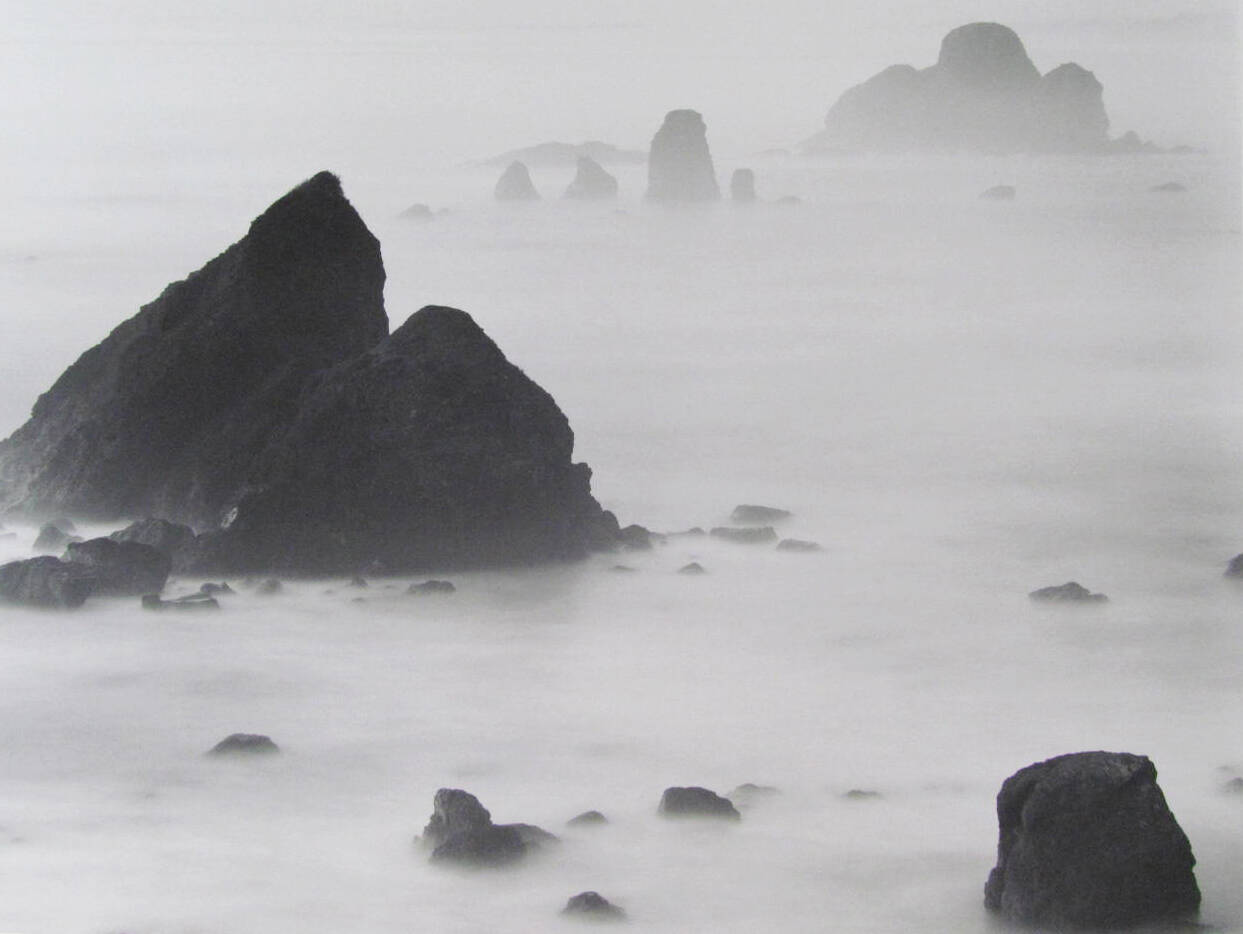 Black and white photograph of large rocks on a beach covered in mist.